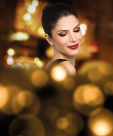 Mujer maquillada sonriendo, luces de fondo.